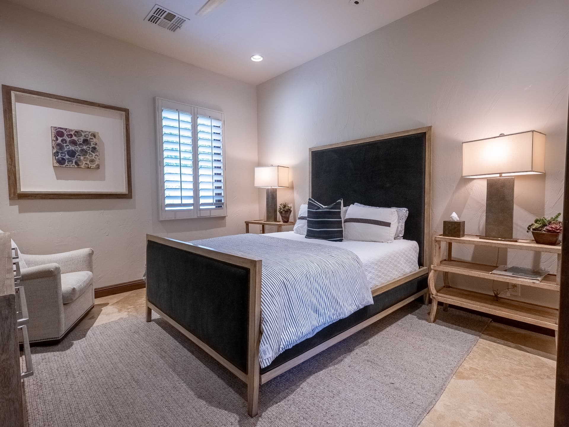 Guest bedroom with velvet upholstered bed, shutters and reading chair