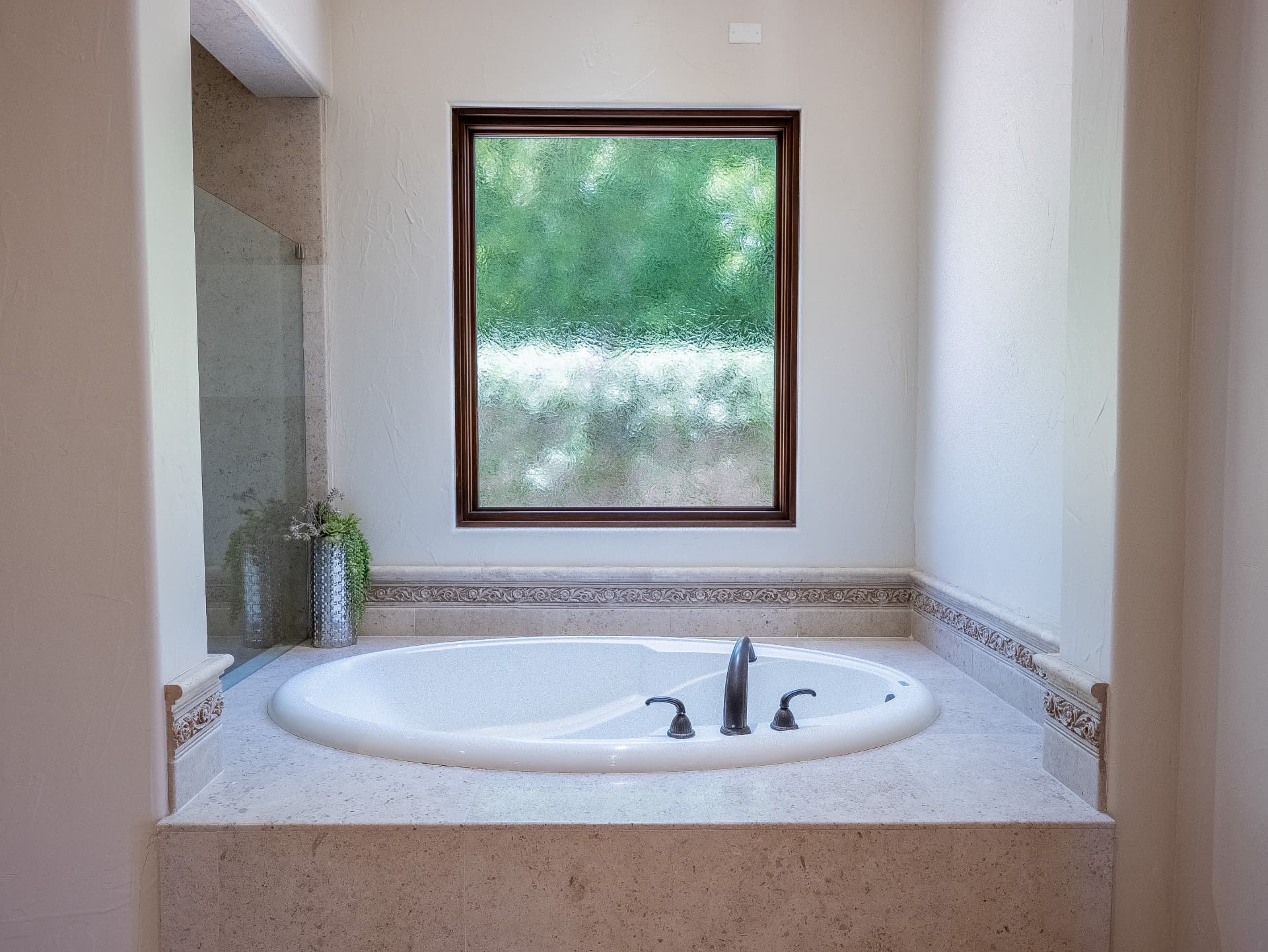 Soaking tub set beneath an obscured glass window in the primary bath