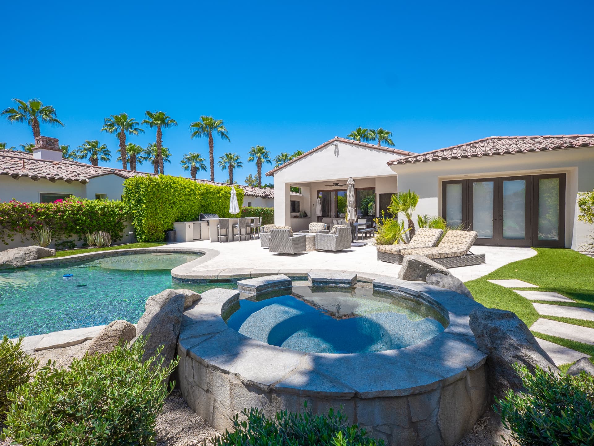 Rock spa and pool with covered patio and palm-lined sky