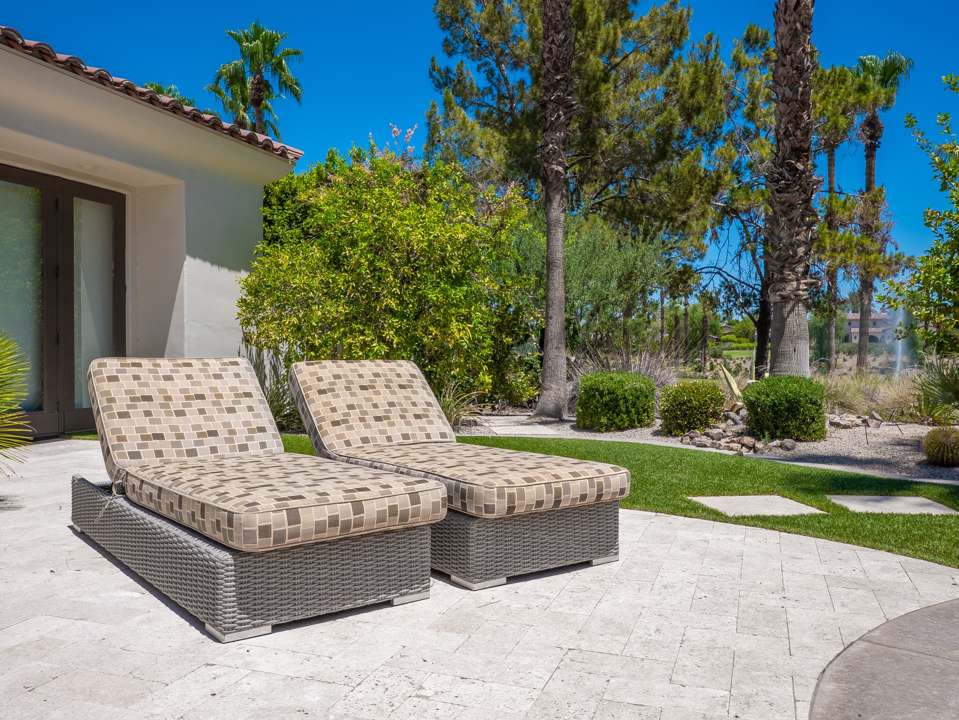 Chaise lounges on the travertine terrace beside manicured lawn