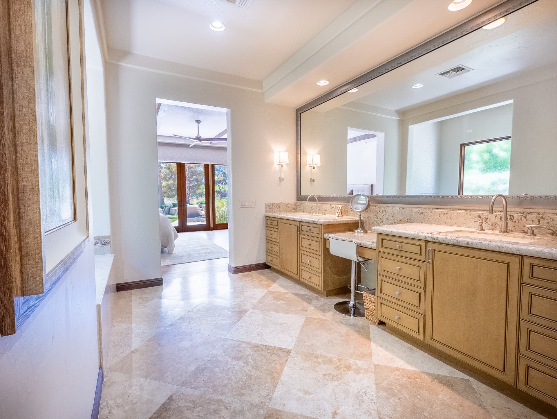 Primary bath with dual vanities, travertine floors and bedroom beyond
