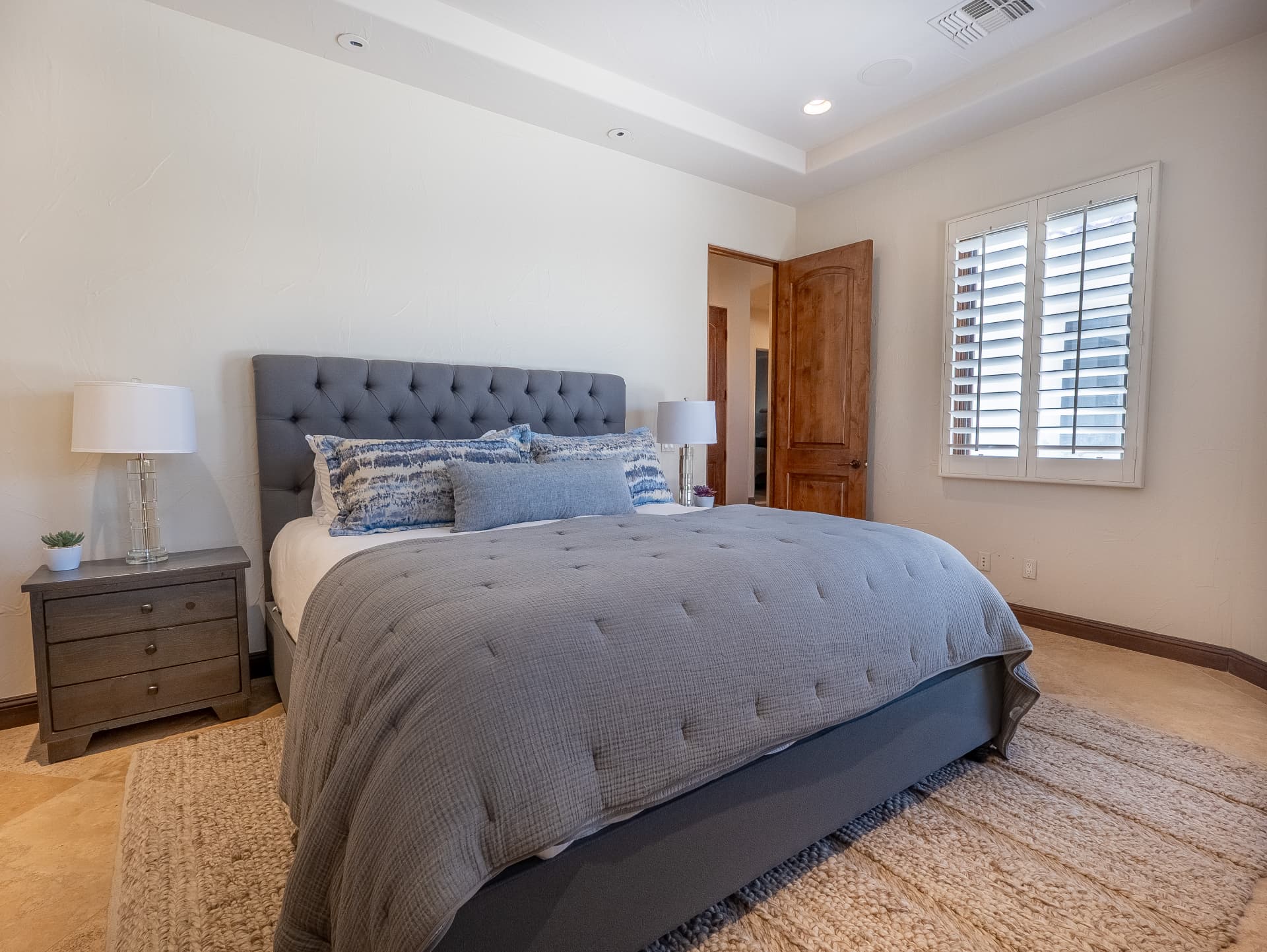 Guest bedroom with tufted headboard, tray ceiling and shutters